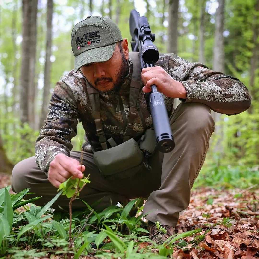 Man in camouflage gear holding a rifle in a forest setting