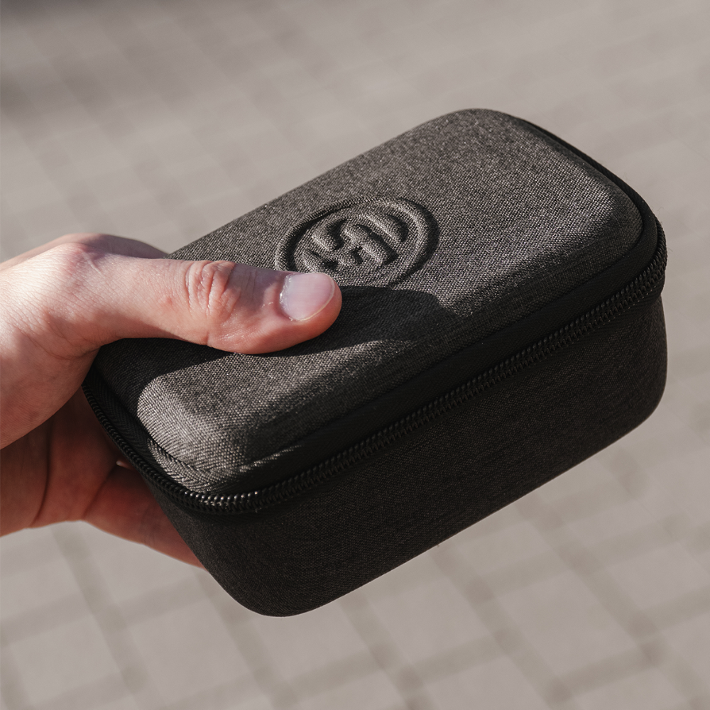 Hand holding a black textured case with a logo on a blurred background